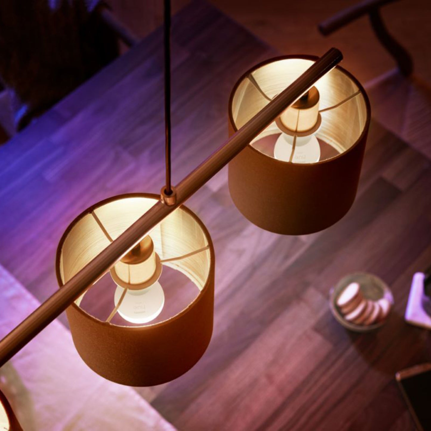 Philips Hue Luster Smart LED-pære E14 470 lm 1-pak i to cylindriske pendellamper over træbord med småkager og serviet.