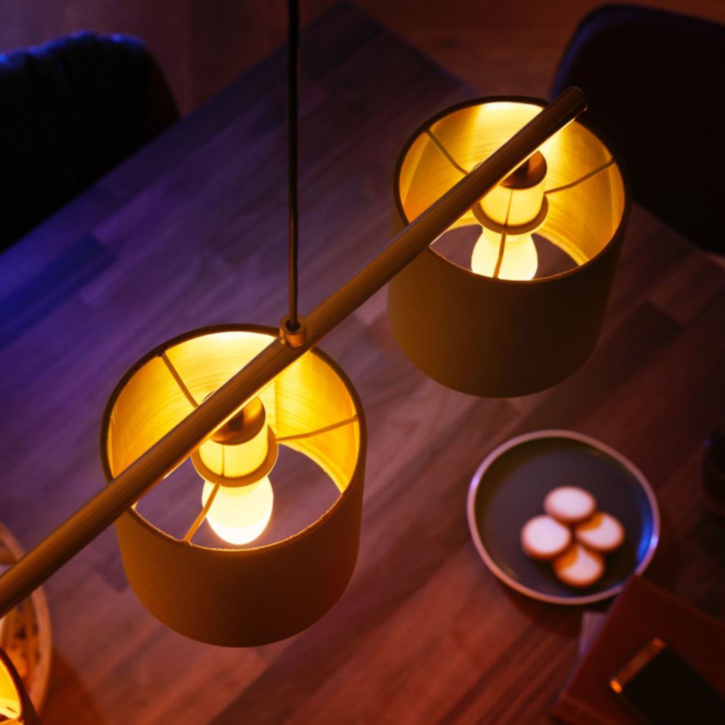 Philips Hue Ambiance Smart LED-pærer E14 470 lm 2-pak lyser gult over træbord med mørk tallerken og fire små runde kager.