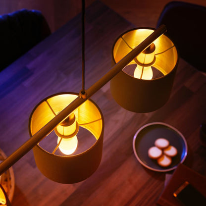 Philips Hue Ambiance Smart LED-pærer E14 470 lm 2-pak lyser gult over træbord med mørk tallerken og fire små runde kager.