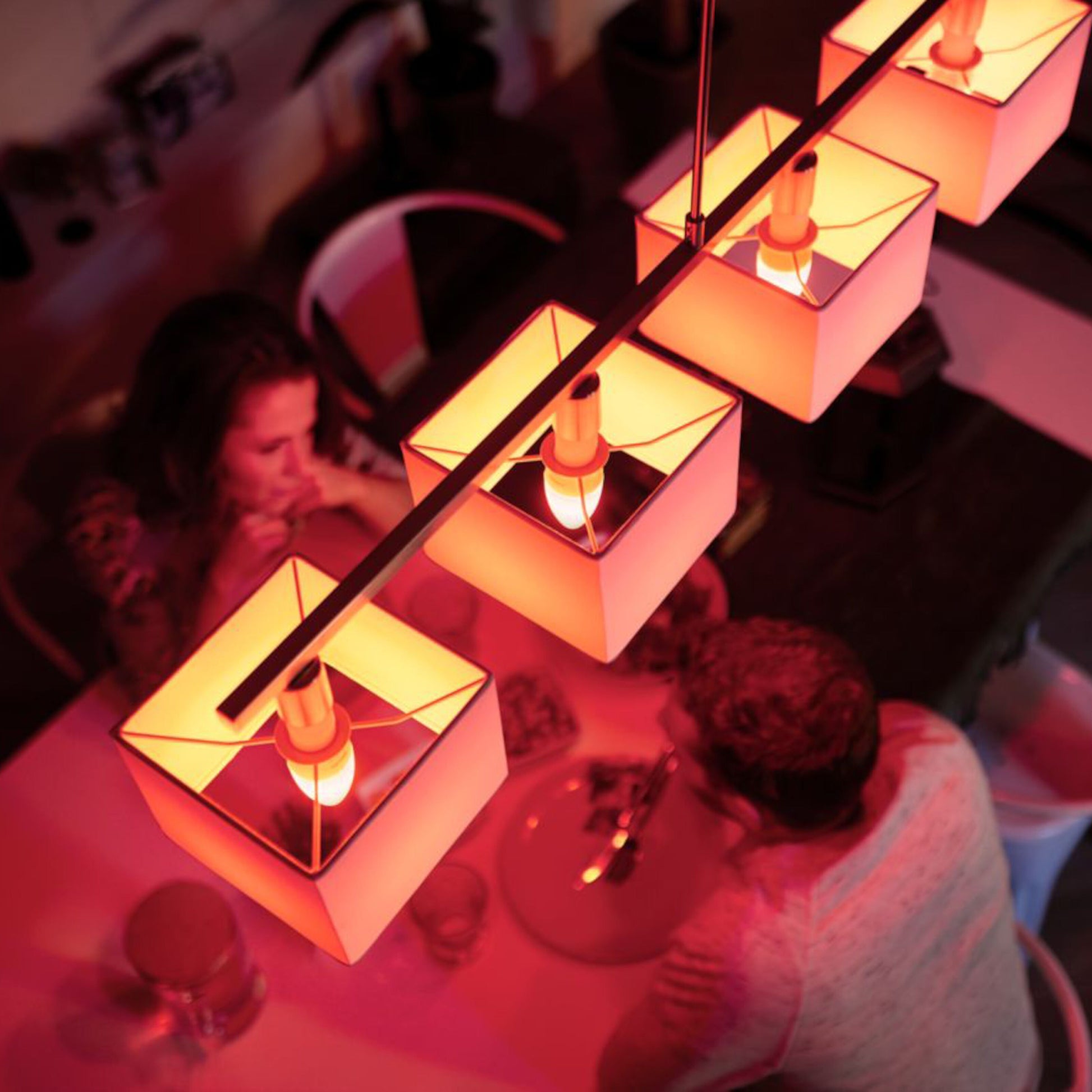 Philips Hue Color Ambiance Smart LED-pære E14 470 lm 2-pack monteret i firkantede pendellamper over spisebord.