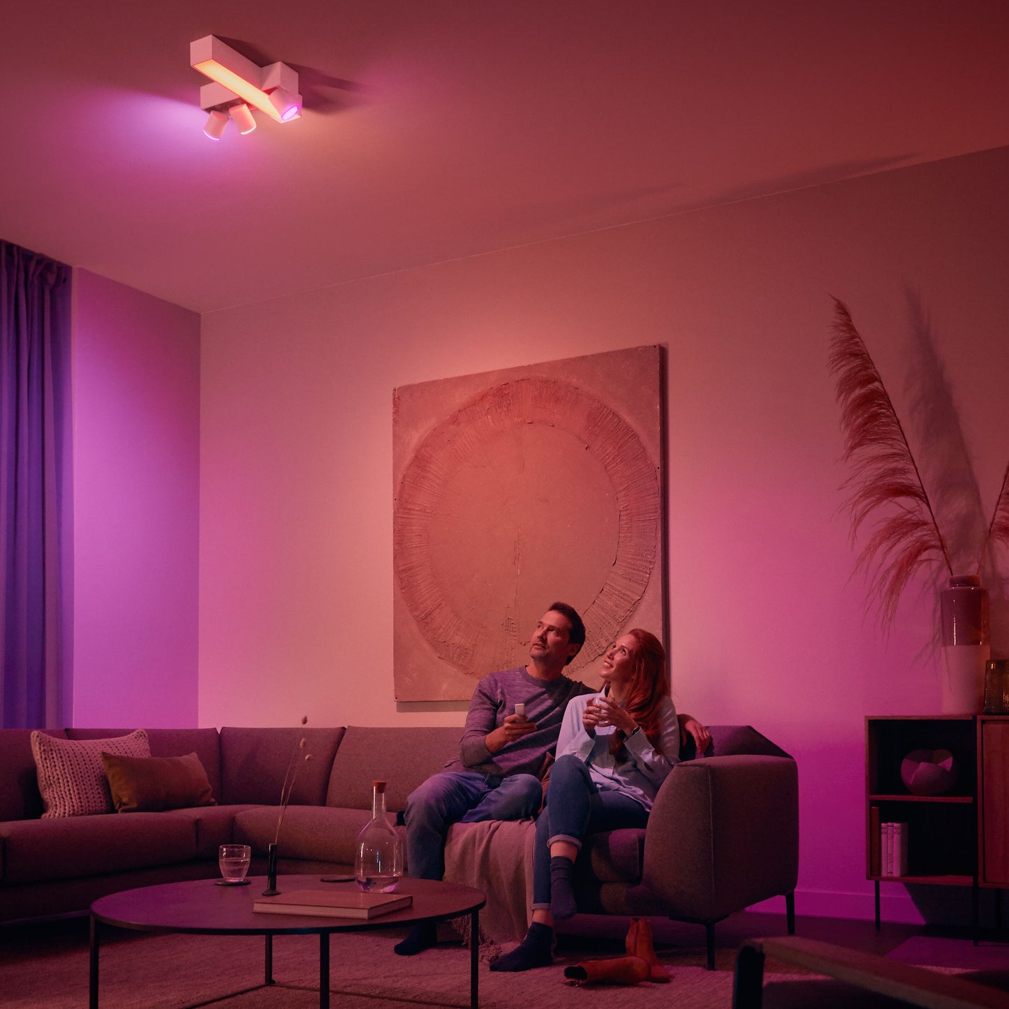 Philips Hue Dim Switch v2 fjernbetjening i stue med pink og lilla lys styret via kontakten, synlig sofa og interiør.