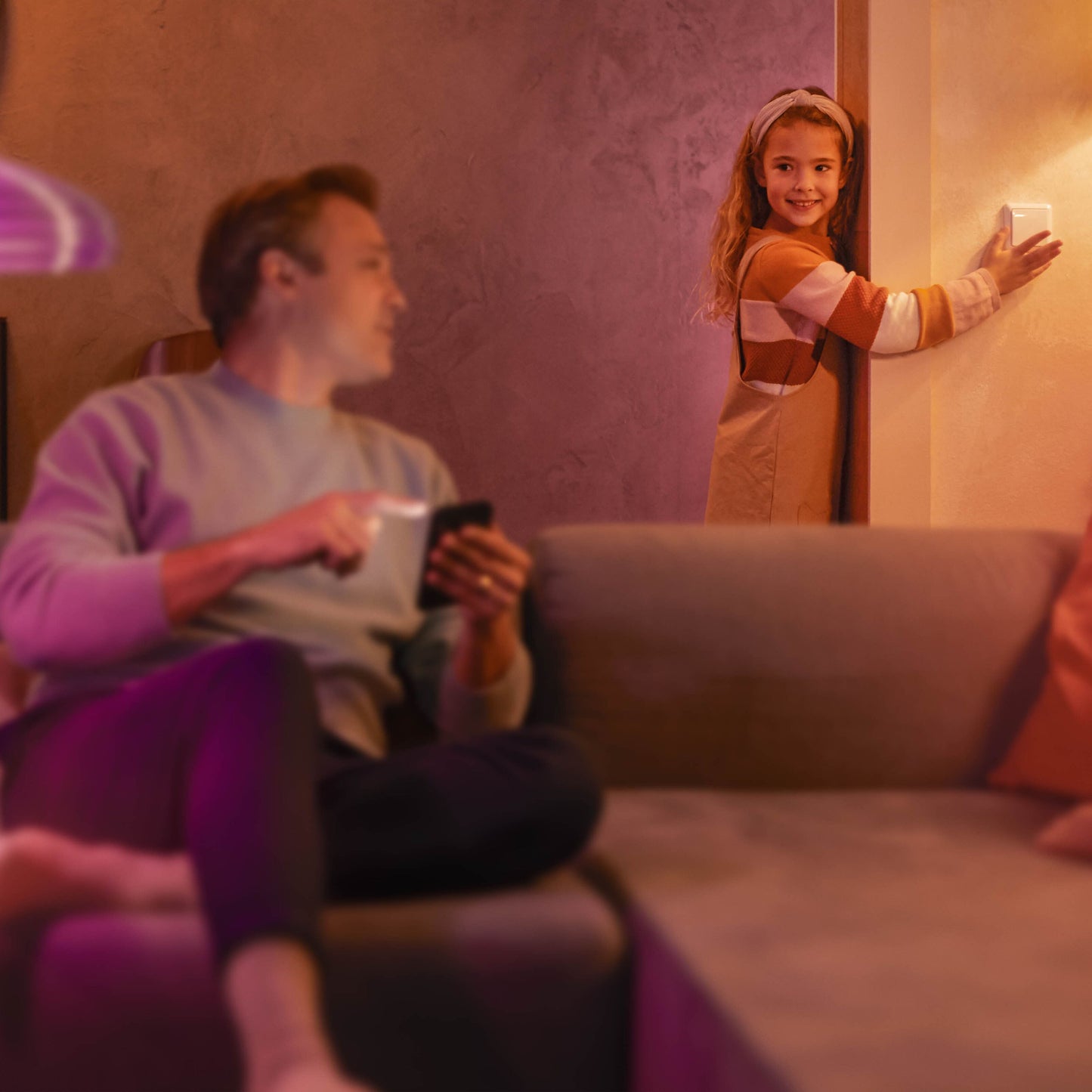 Philips Hue Vægafbrydermodul justeres af barn i stue, voksen med smartphone synlig i baggrunden.