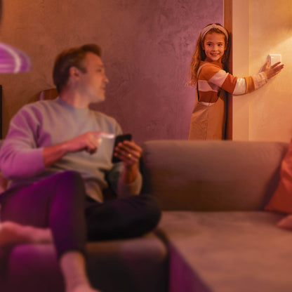 Philips Hue Vægafbrydermodul justeres af barn i stue, voksen med smartphone synlig i baggrunden.