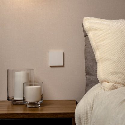 Aqara Smart vægkontakt H1 Dobbelt uden nulleder Zigbee 3.0 monteret over natbord ved seng med cremefarvet sengetøj.