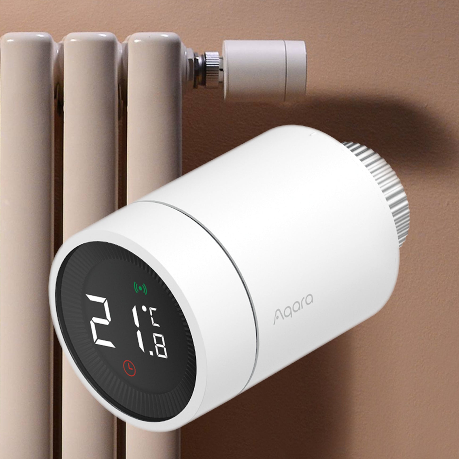 Aqara E1 Smart Termostat til radiator med digitalt display viser 21°C, monteret på radiator mod brun væg.