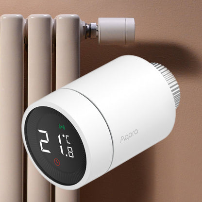 Aqara E1 Smart Termostat til radiator med digitalt display viser 21°C, monteret på radiator mod brun væg.
