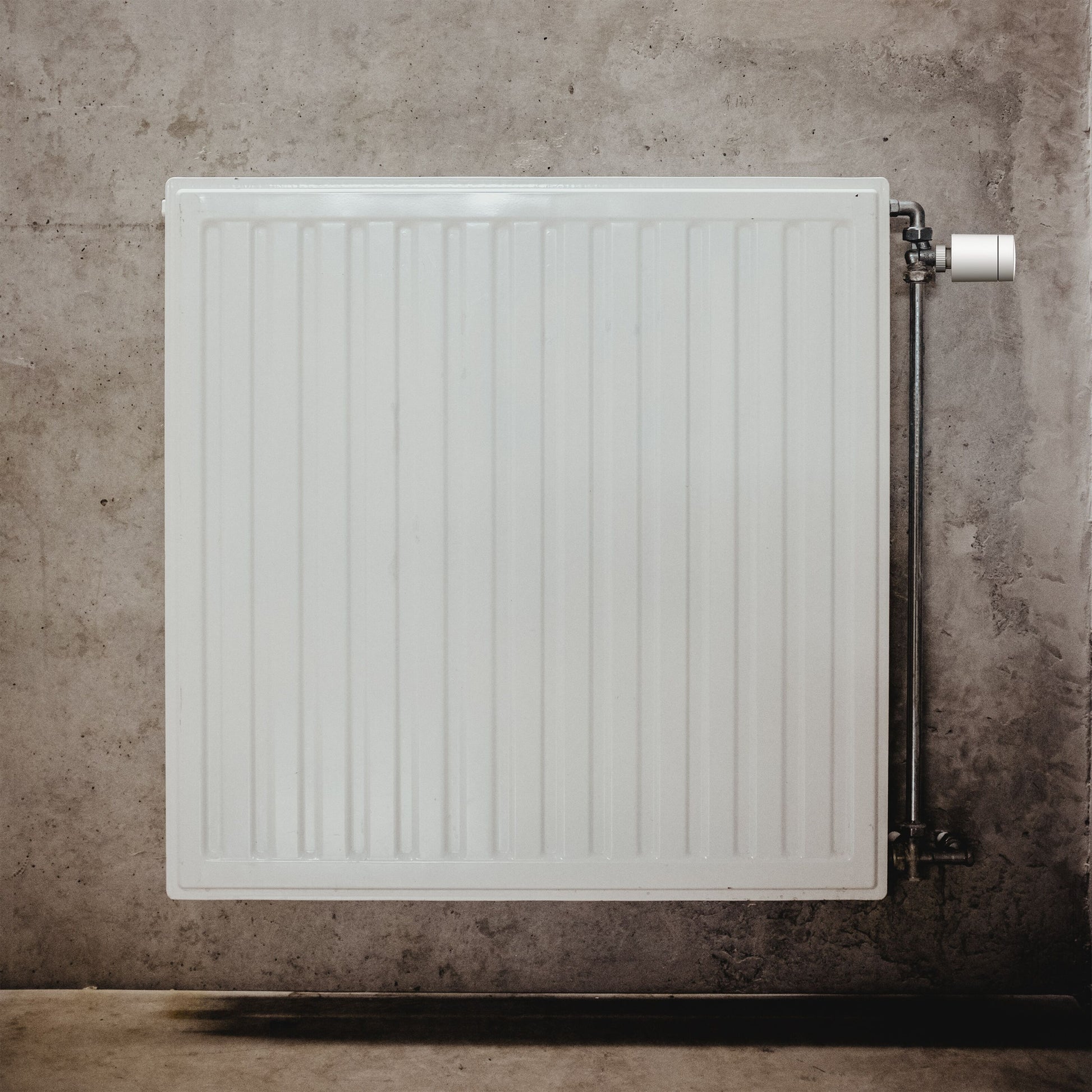 Aqara E1 Smart Termostat til radiatorer monteret på hvid radiator med metalrør og reguleringsventil på højre side.