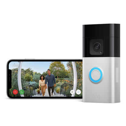 Ring Batteridørklokke Plus ved siden af smartphone med livevideo af to personer ved grøn udendørs indgang.