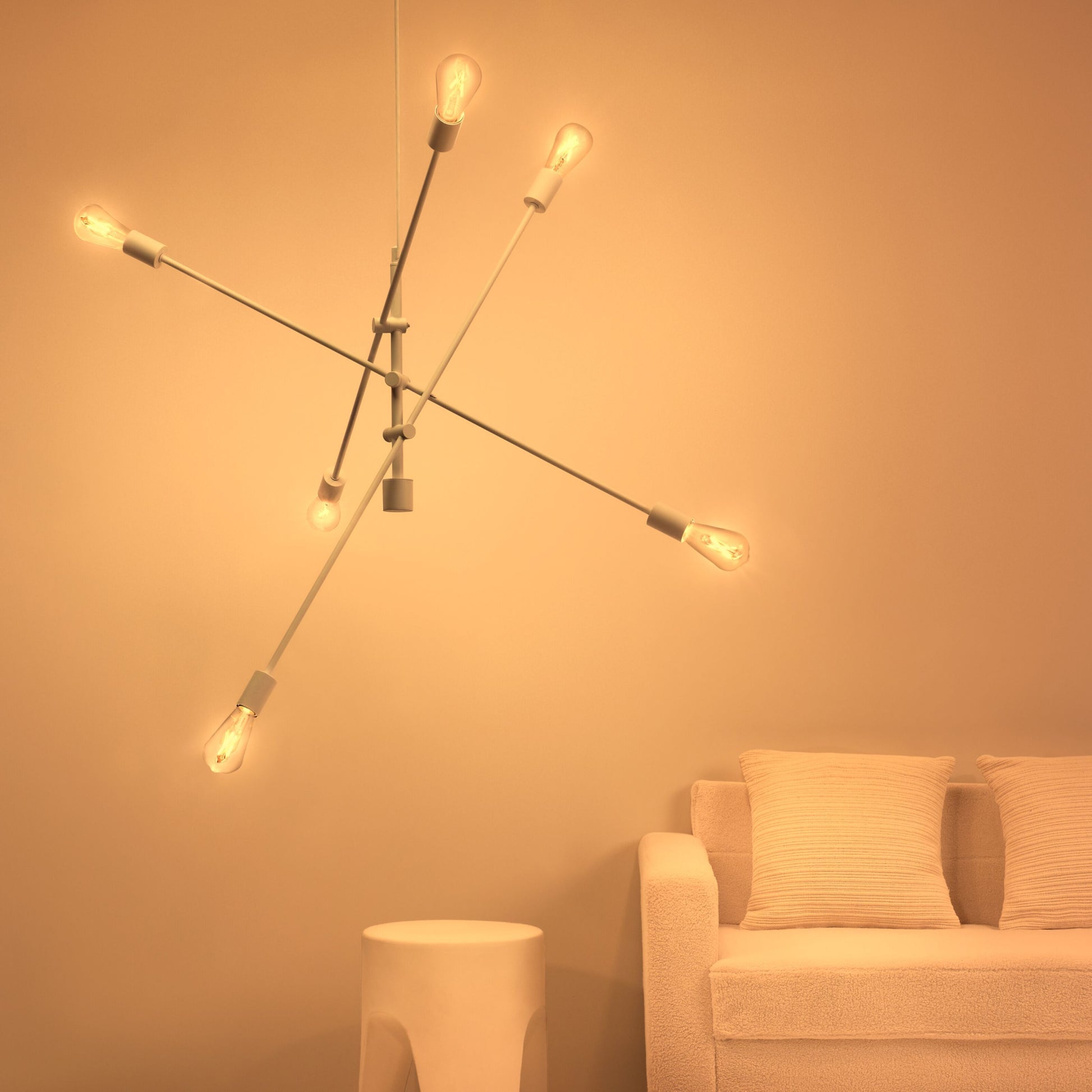 WiZ Amber Filament A60 Smart LED-pære E27 640 lm i geometrisk loftslampe over beige sofa med to puder og lille rund sidebord.