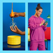 WiZ Klar Filament G95 Smart LED-pære E27 806 lm installeres i gul lampe, appstyret belysning vises ved smartphone.