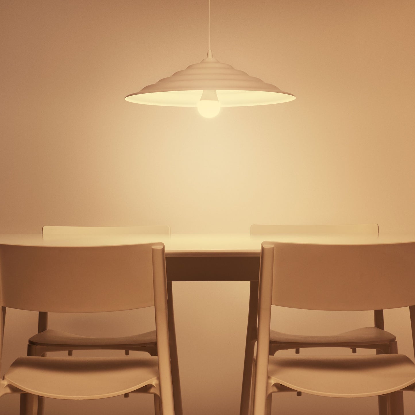WiZ Farve Høj Lumen A80 Smart LED-pære E27 2452 lm over bord med to lyse stole, beige væg baggrund.