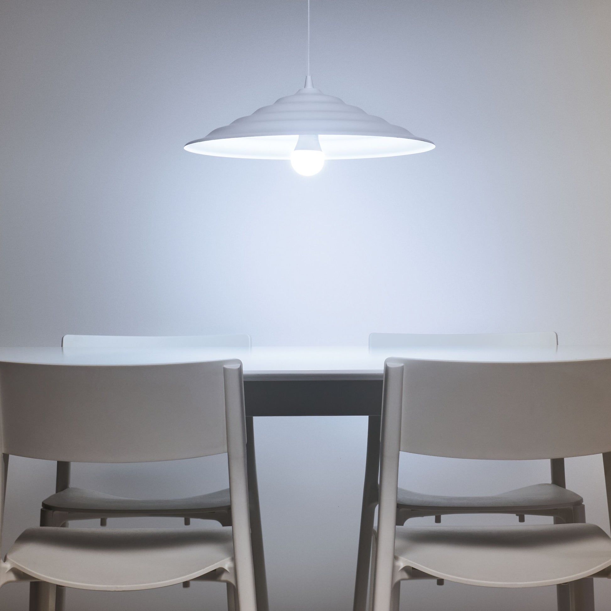 WiZ Farve Høj Lumen A80 Smart LED-pære E27 2452 lm i pendel over hvidt bord og to hvide stole mod lys grå væg.