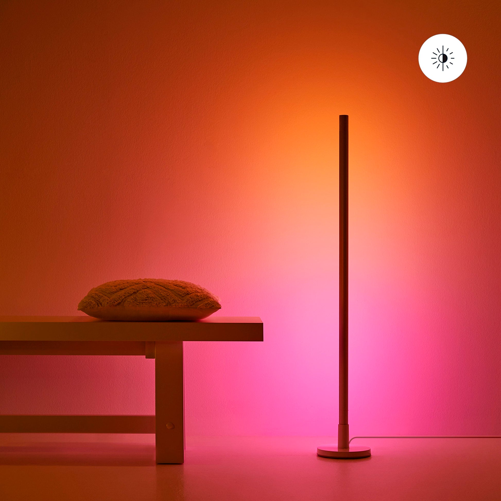 WiZ Stolpe Gulvlampe gulvbelysning med varm rosa-orange lys, synlig pæreikon for smart belysning, lav bænk og pude.