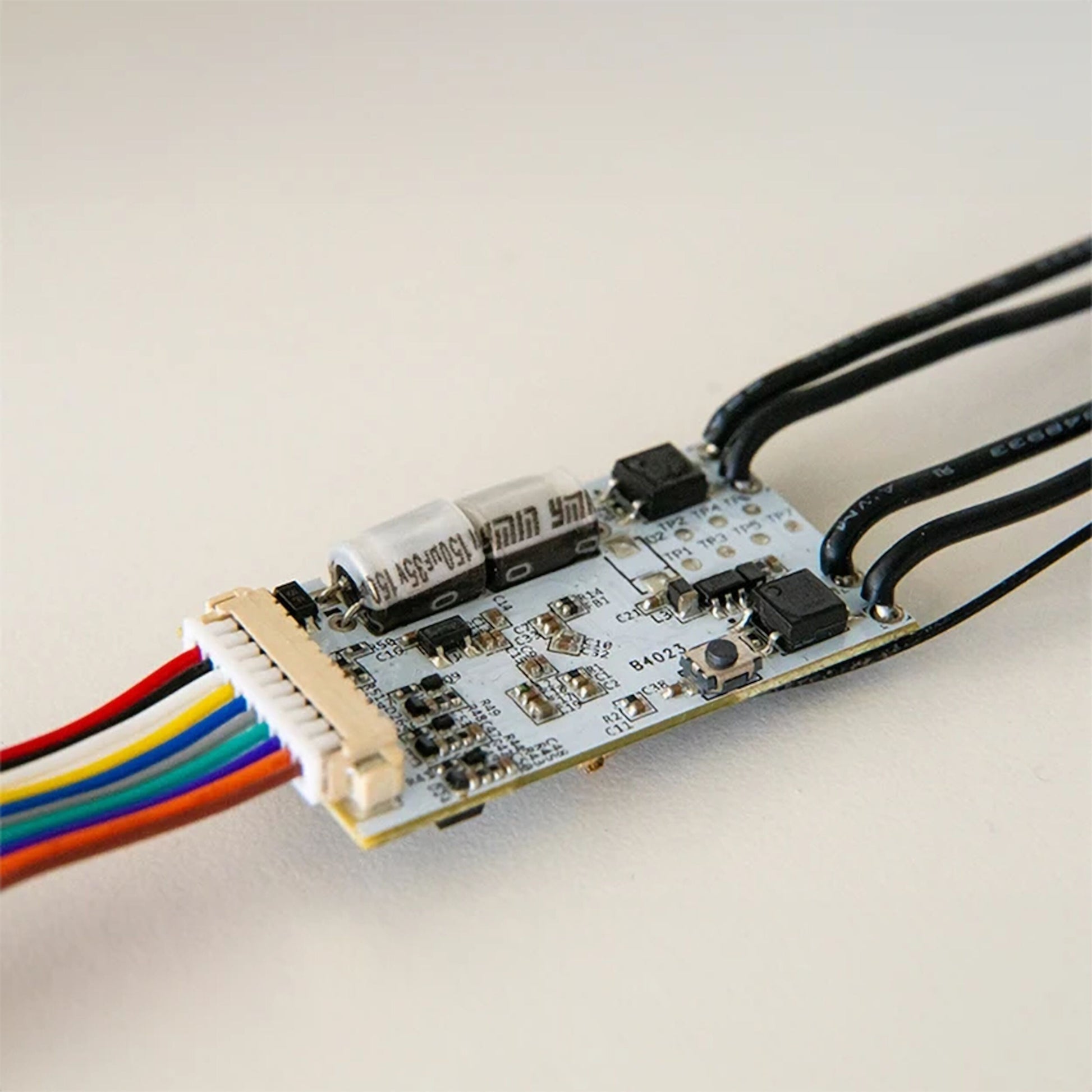 Shelly Plus Uni Smart Wifi-modul, nærbillede af kondensatorer, mikrochips, sorte kabler og flerfarvet båndkabel.