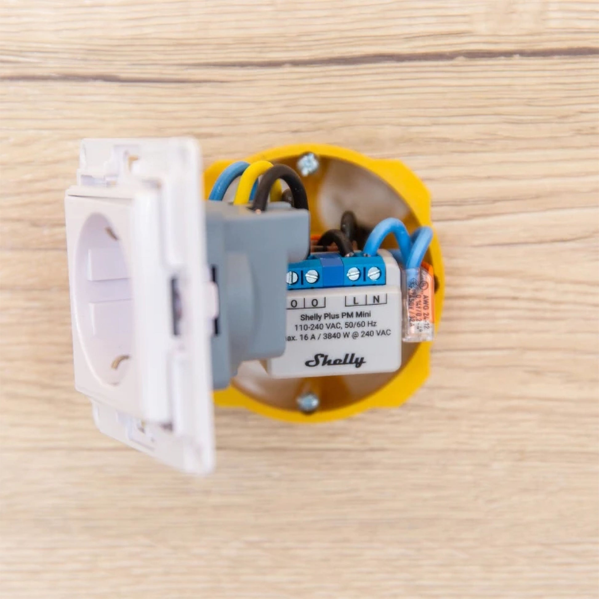 Shelly PM Mini GEN 3 WiFi effektmåler i gul el-boks med synlige ledninger monteret på trævæg.
