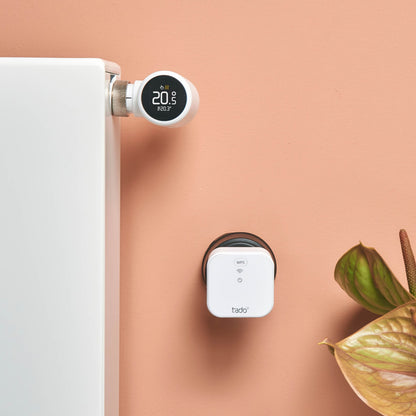 Tado Bro X grænserouter smart radiatortermostat Matter-over-Thread 20,5°C på hvid radiator ved ferskenfarvet væg.