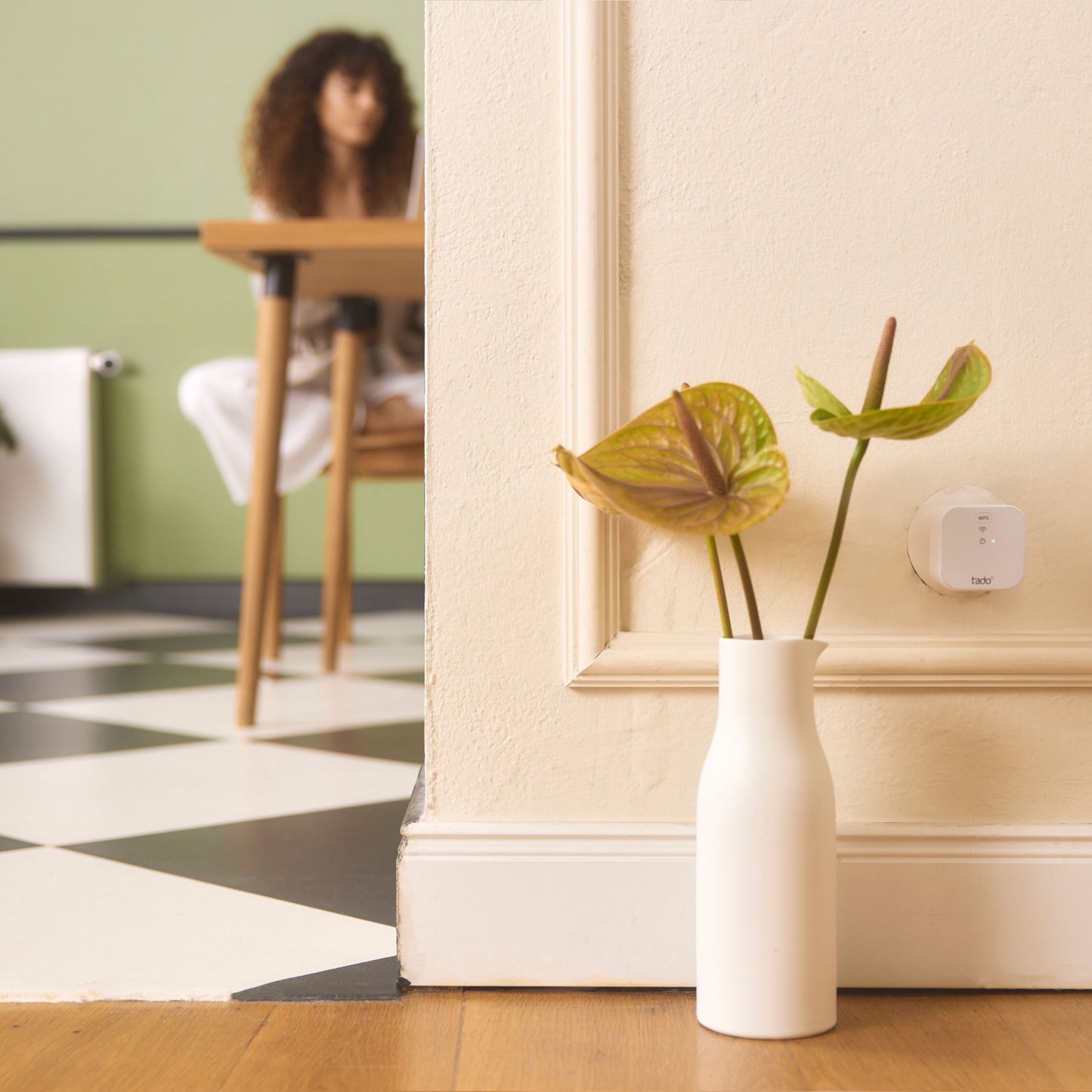 Hvid vase med grønne anthuriumblomster ved siden af Tado Bro X grænserouter og andre smart home-enheder på sort-hvidt gulv.
