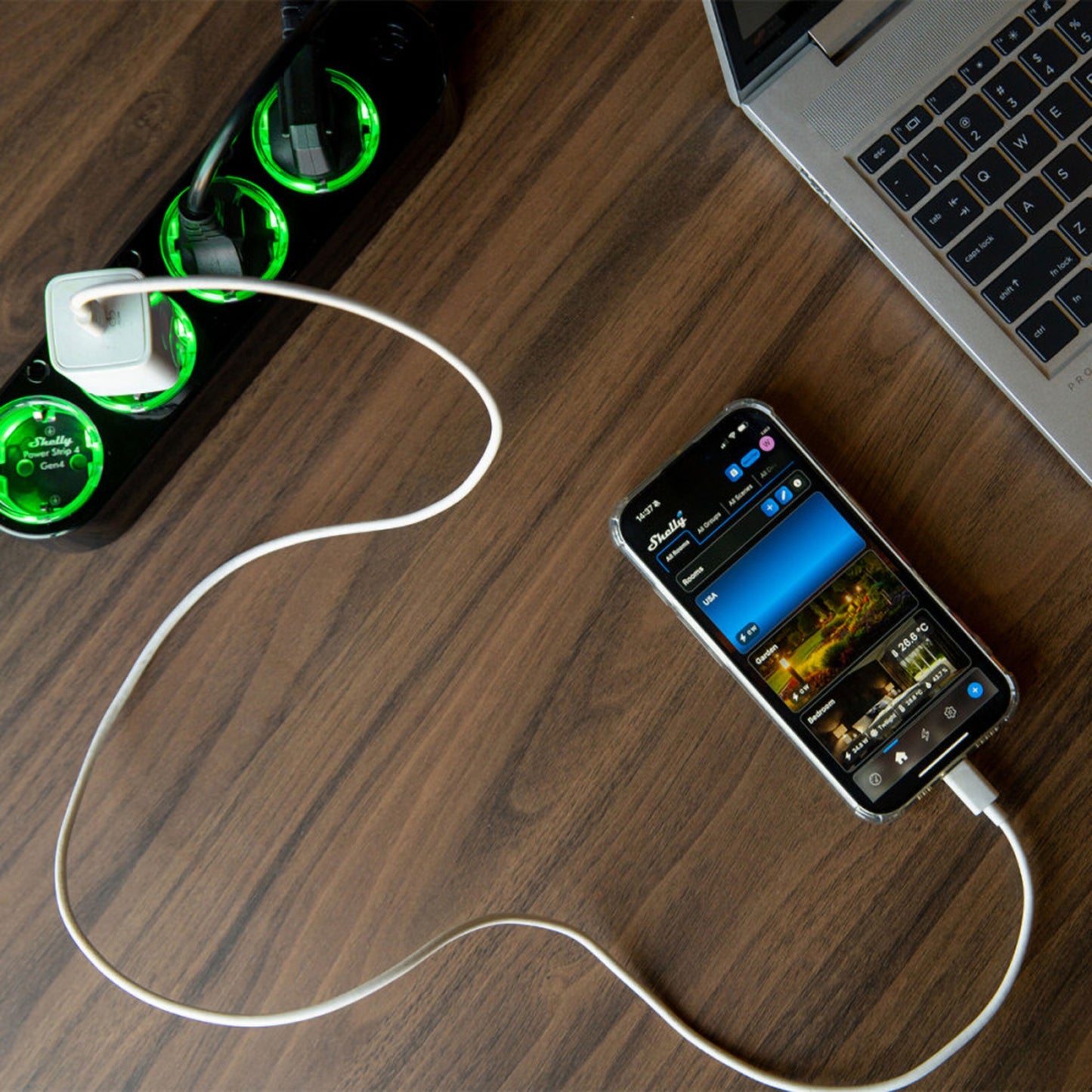 Shelly Strømfordeler 4 Gen4 sort smart strømfordeler med grønne LED-udtag, smartphone oplades via hvidt kabel.