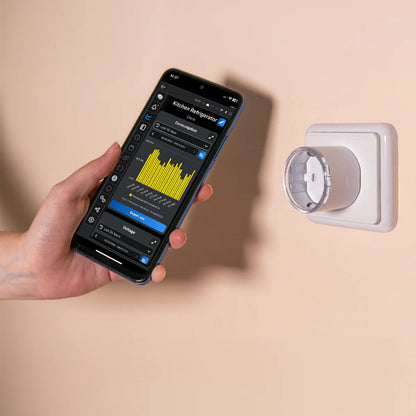 Shelly Plug S Gen3 smart stik Hvid i stikkontakt, smartphone viser energimåling data, hånd holder telefonen.