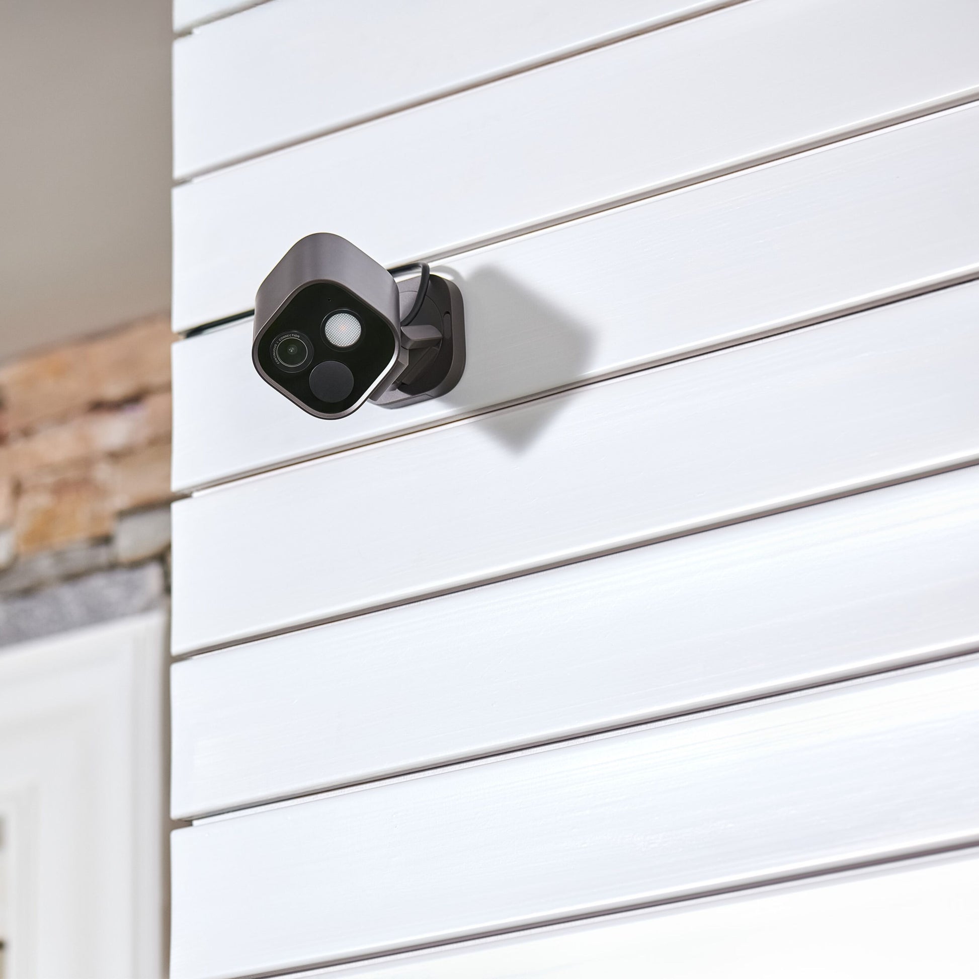 Aqara Camera Hub G5 Pro WiFi, hvid, monteret indendørs på hvid vandret panelvæg tæt ved synligt mursten.