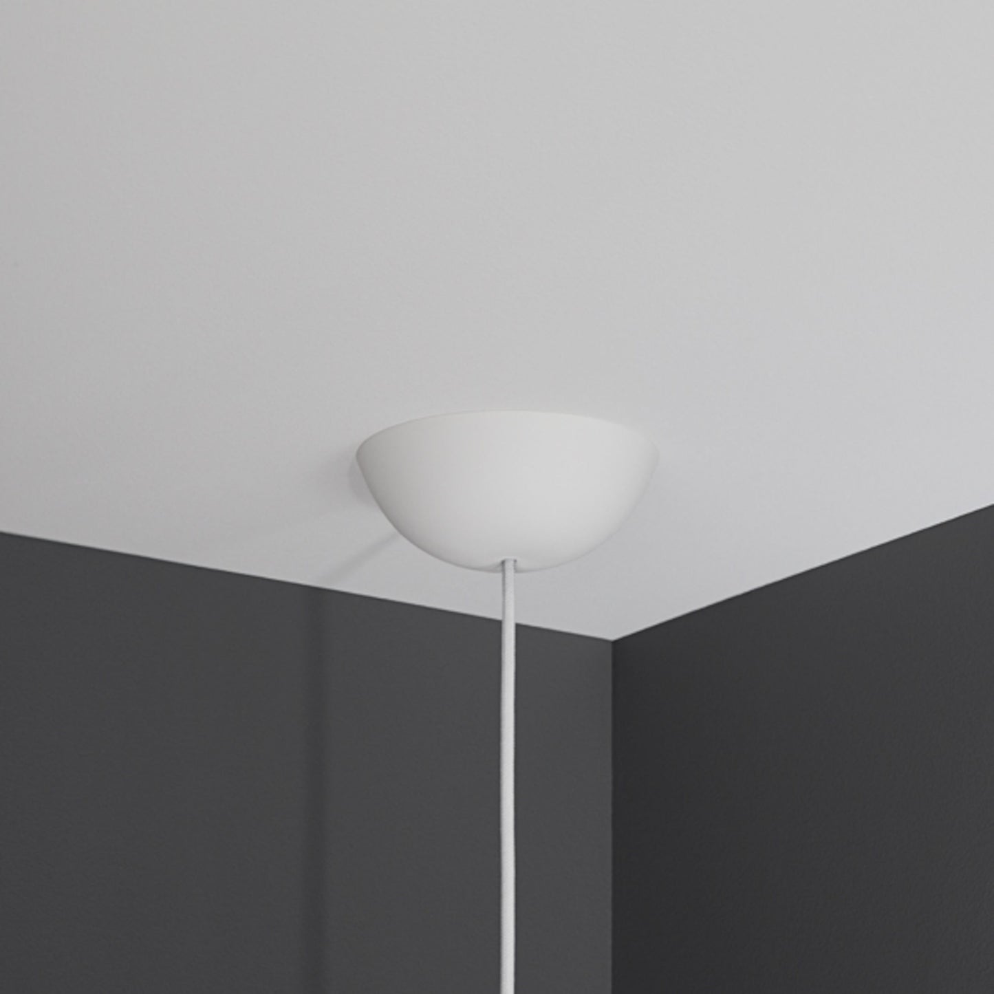 Cablecup Klassisk loftroset hvid Ø158 mm med ledning monteret i hjørnet mellem hvidt loft og to mørkegrå vægge.