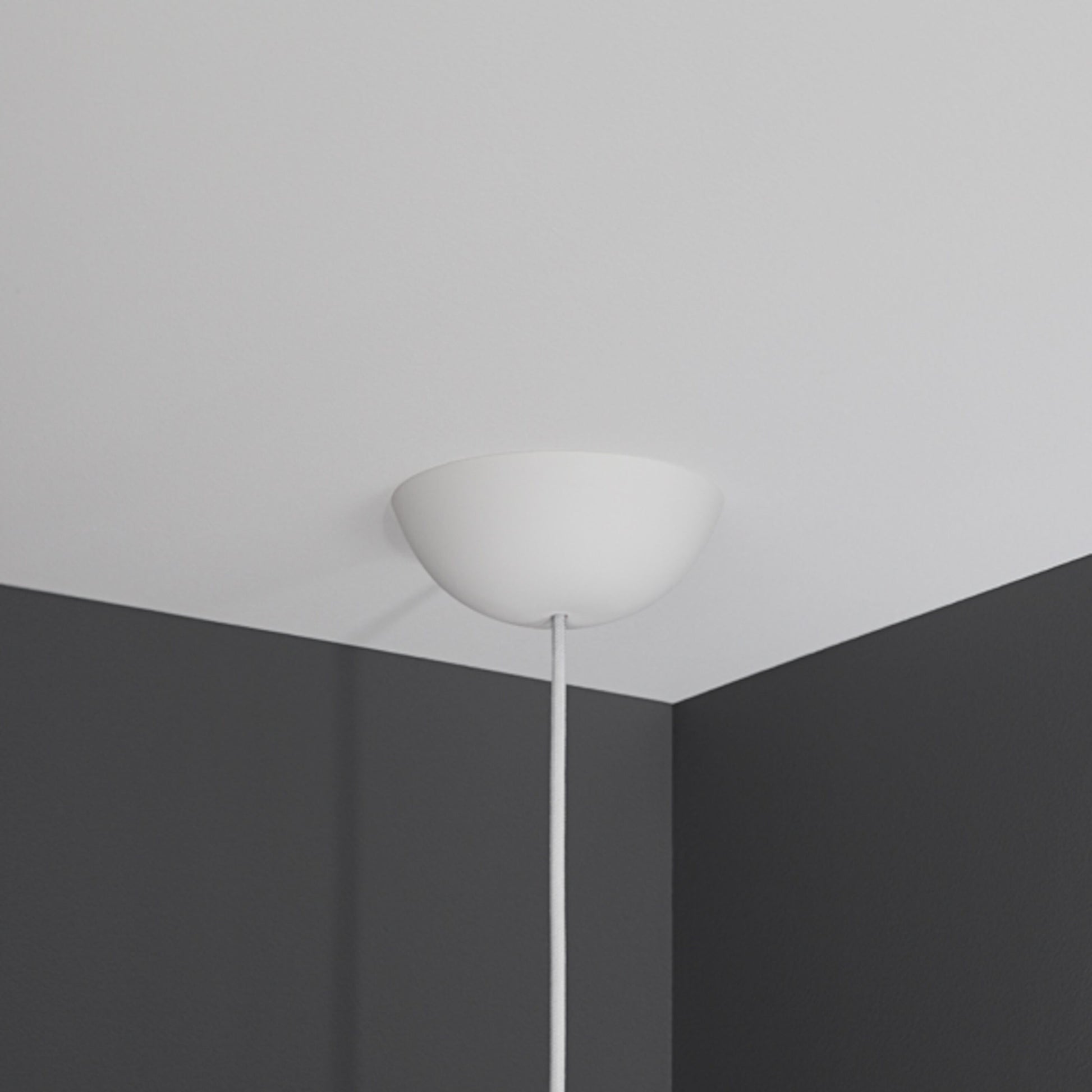 Cablecup Klassisk loftroset hvid Ø158 mm med ledning monteret i hjørnet mellem hvidt loft og to mørkegrå vægge.
