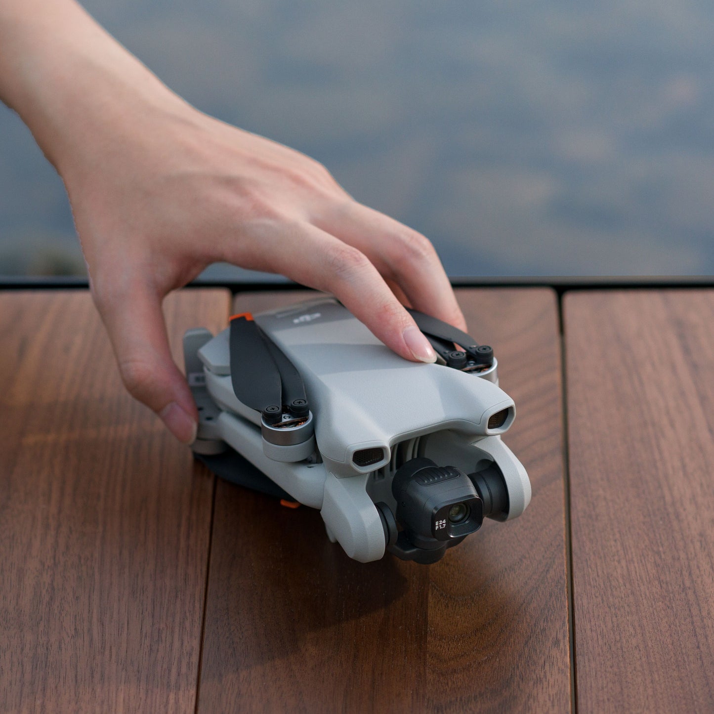 DJI Mini 3 drone sammenfoldet med 4K kamera, hånd holder enheden på træoverflade.