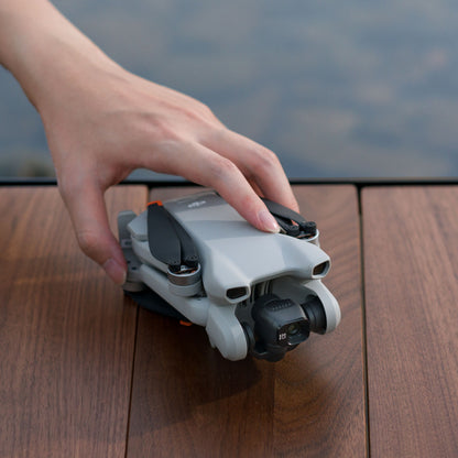 DJI Mini 3 drone sammenfoldet med 4K kamera, hånd holder enheden på træoverflade.