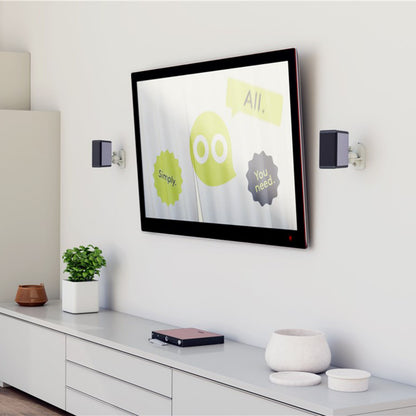 Goobay 2-pak højttalerbeslag hvid monteret ved TV over hvidt skab med plante og bog, optimal placering vises.