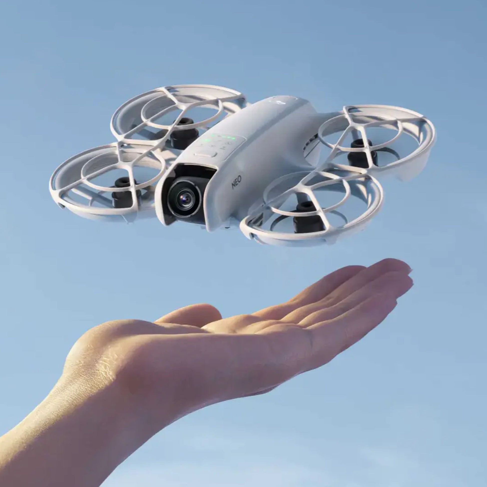 DJI Neo Motion Fly More Combo 4K drone med fire propeller ses svævende over hånd mod blå baggrund.