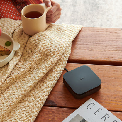 Aqara Hub M3 Smart Home Controller ved siden af sort Poco enhed, beige strikket tæppe, magasin delvist synlig på bord.