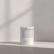 Aqara Bevægelses- og lyssensor AS5, kompakt cylindrisk design, hvid, stående på lyst underlag mod neutral væg.