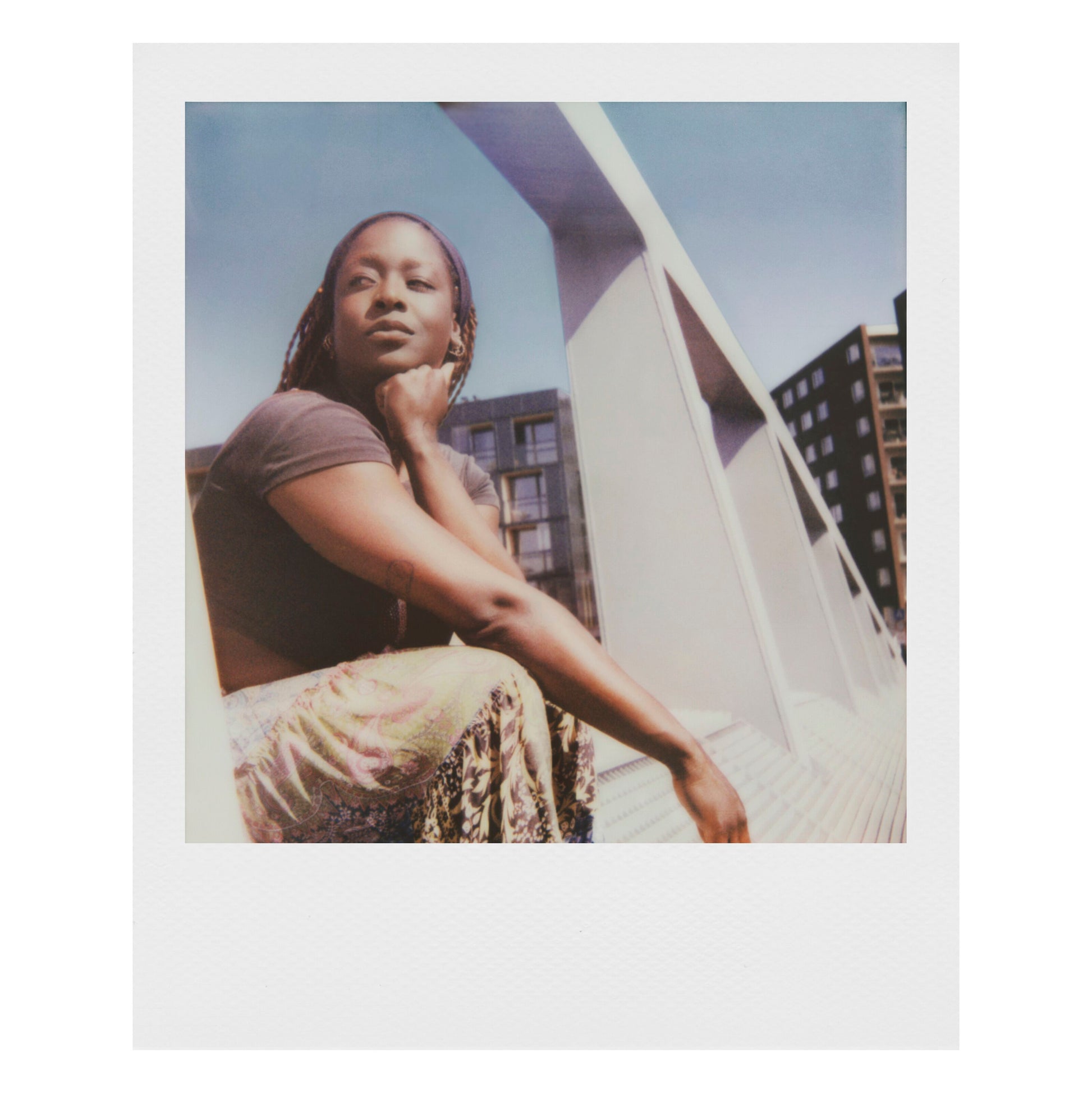 Polaroid Now Gen 3 Sort med film ligger ved siden af kvinde udendørs, kamera og emballage tydeligt synlige.