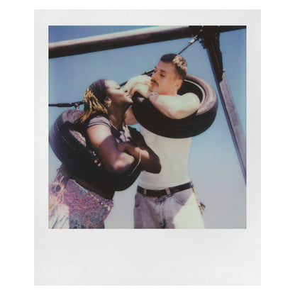Polaroid Now Gen 3 Sort med film fanger to personer med billedækgynger tæt sammen under blå himmel.