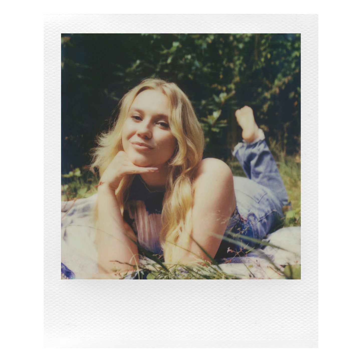 Polaroid Now Gen 3 Sort med film ses i brug udendørs, kvinde med langt lyst hår på tæppe, omgivet af grønt.