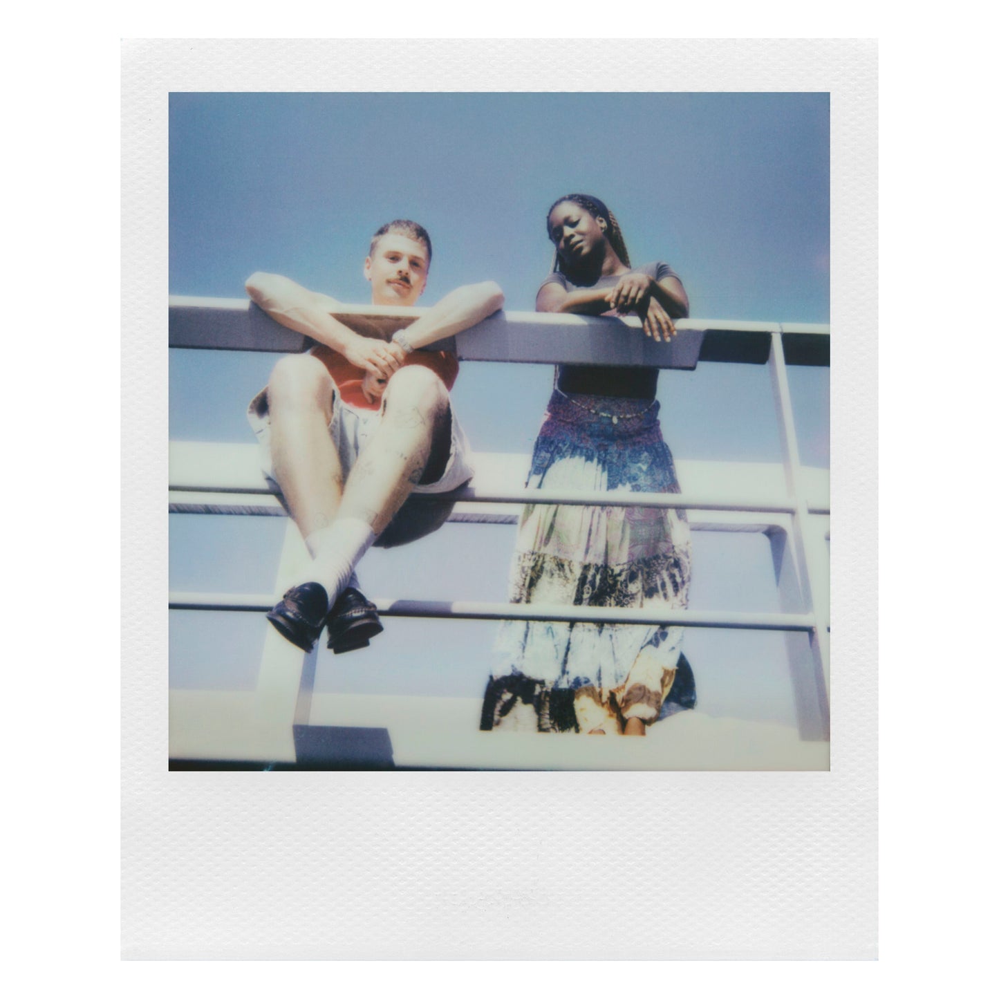 Polaroid Now Gen 3 Sort analog instantkamera med film brugt udendørs, personer i motivet, blå himmel som baggrund.