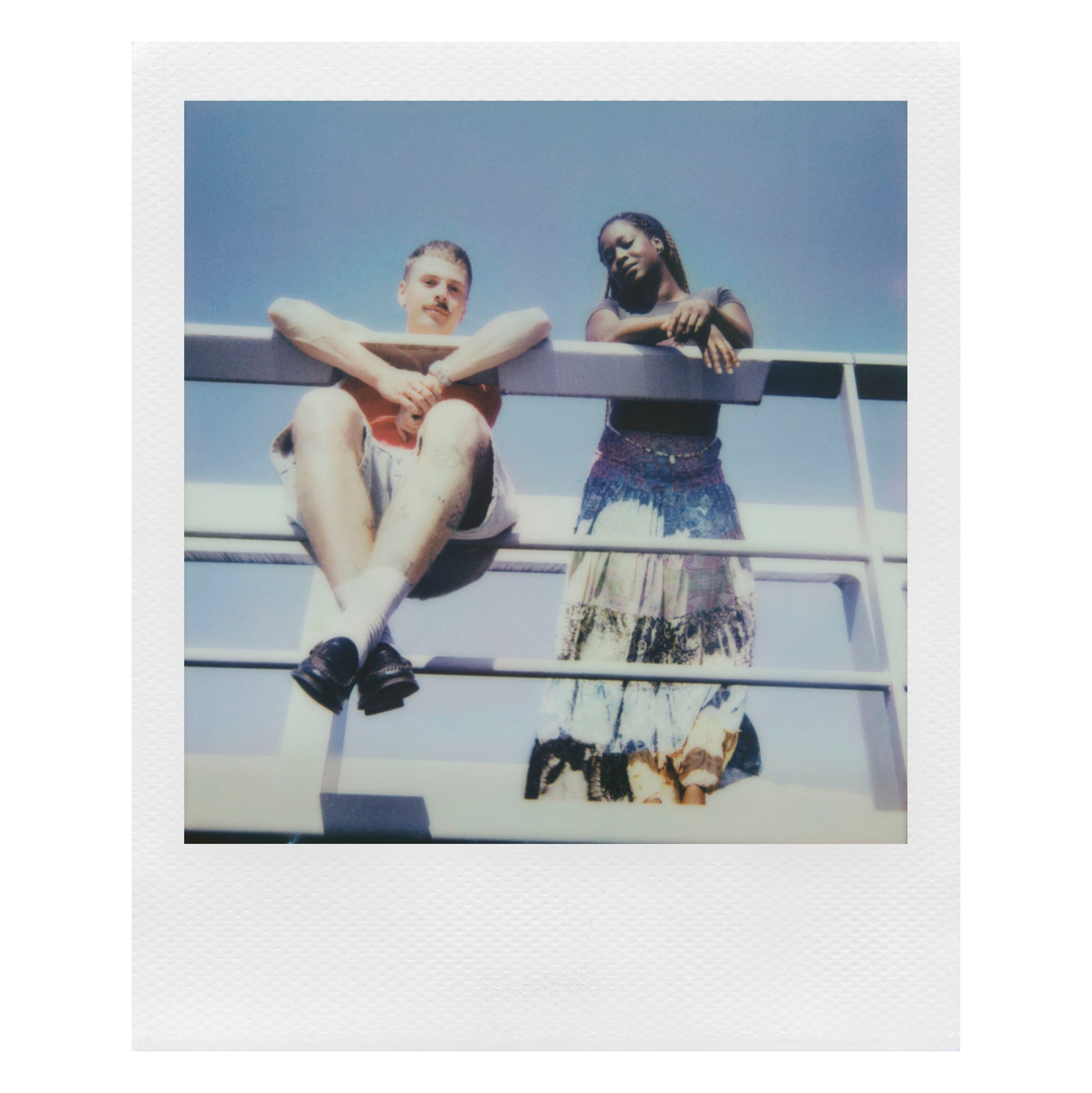 Polaroid Now Gen 3 Sort analog instantkamera med film brugt udendørs, personer i motivet, blå himmel som baggrund.
