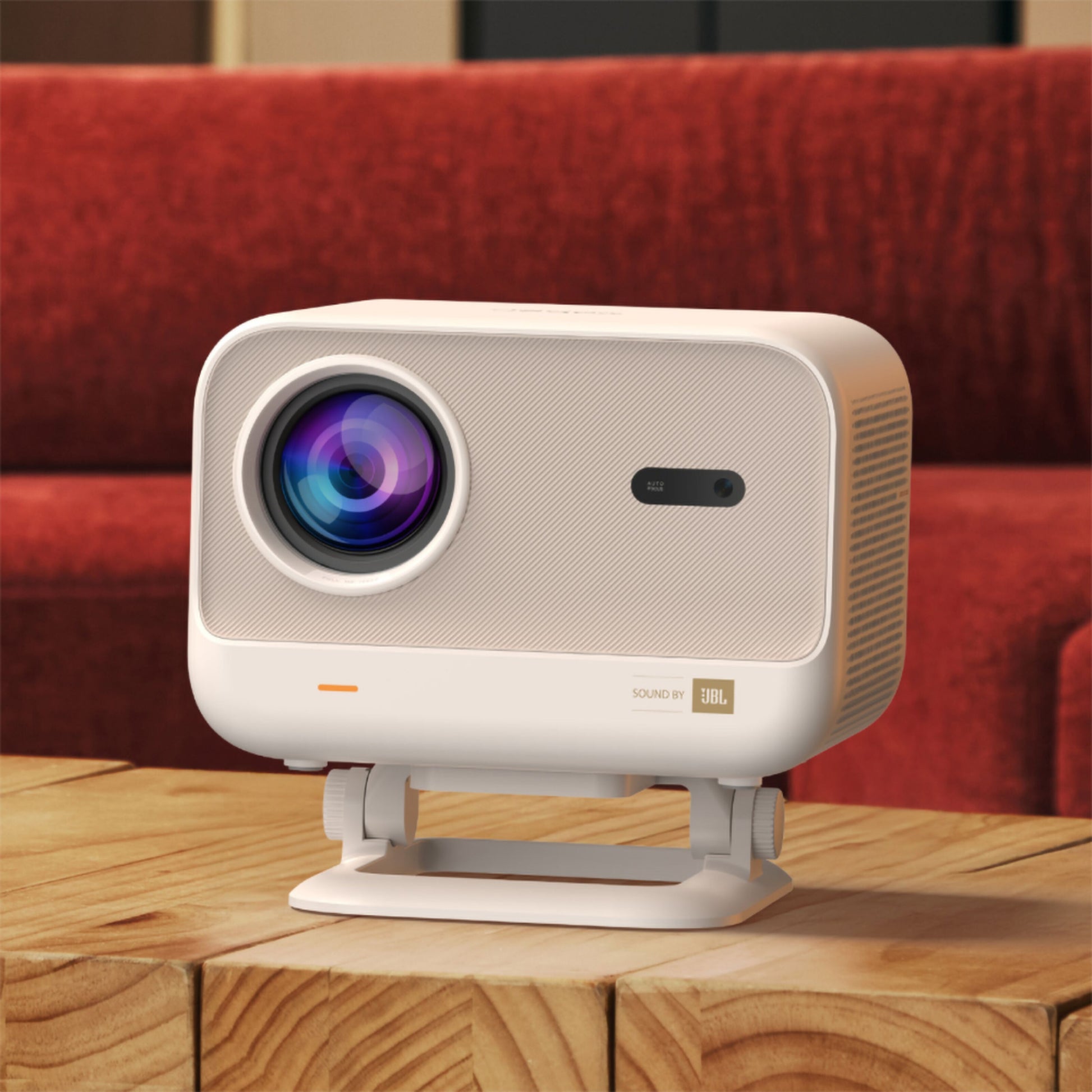 Yaber L2 Plus Full HD projektor med tydelig linse og JBL lydlogo på træbord, rød sofa synlig i baggrunden.