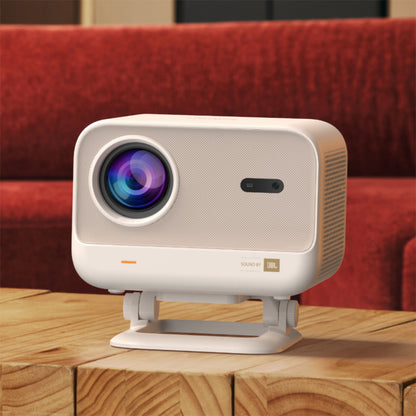 Yaber L2 Plus Full HD projektor med tydelig linse og JBL lydlogo på træbord, rød sofa synlig i baggrunden.