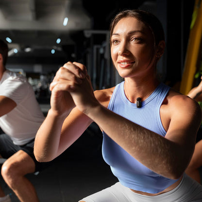 Boya mini 2 trådløst mikrofonsystem til iPhone bæres af kvinde under træning i fitnesscenter, blå top, hvide shorts.