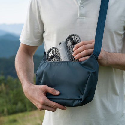 DJI Neo 2 Fly More Combo RC-N3 drone, kompakt, hvid skjorte, blå skuldertaske, grønne bakker i baggrunden.