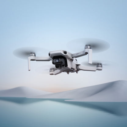 DJI Mini 4K Fly More Combo drone svæver over vand med sneklædte bakker i baggrunden, kompakt model med 4K-video.