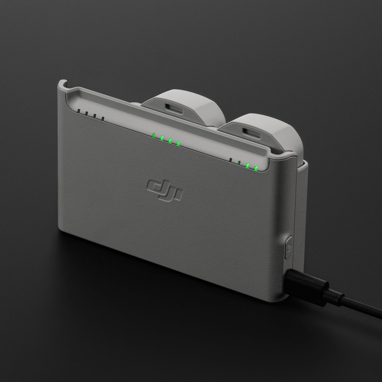 DJI Neo opladningsstation i grå med to batterier isat, tilsluttet strøm, grønne indikatorlys synlige.