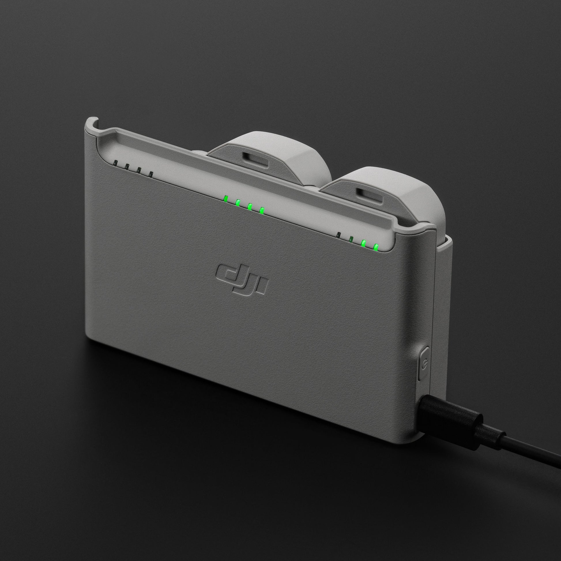 DJI Neo opladningsstation i grå med to batterier isat, tilsluttet strøm, grønne indikatorlys synlige.