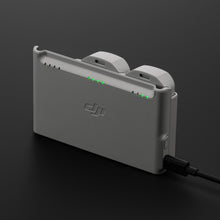 DJI Neo opladningsstation i grå med to batterier isat, tilsluttet strøm, grønne indikatorlys synlige.