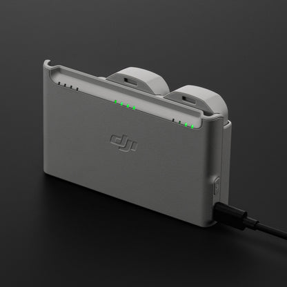 DJI Neo opladningsstation i grå med to batterier isat, tilsluttet strøm, grønne indikatorlys synlige.