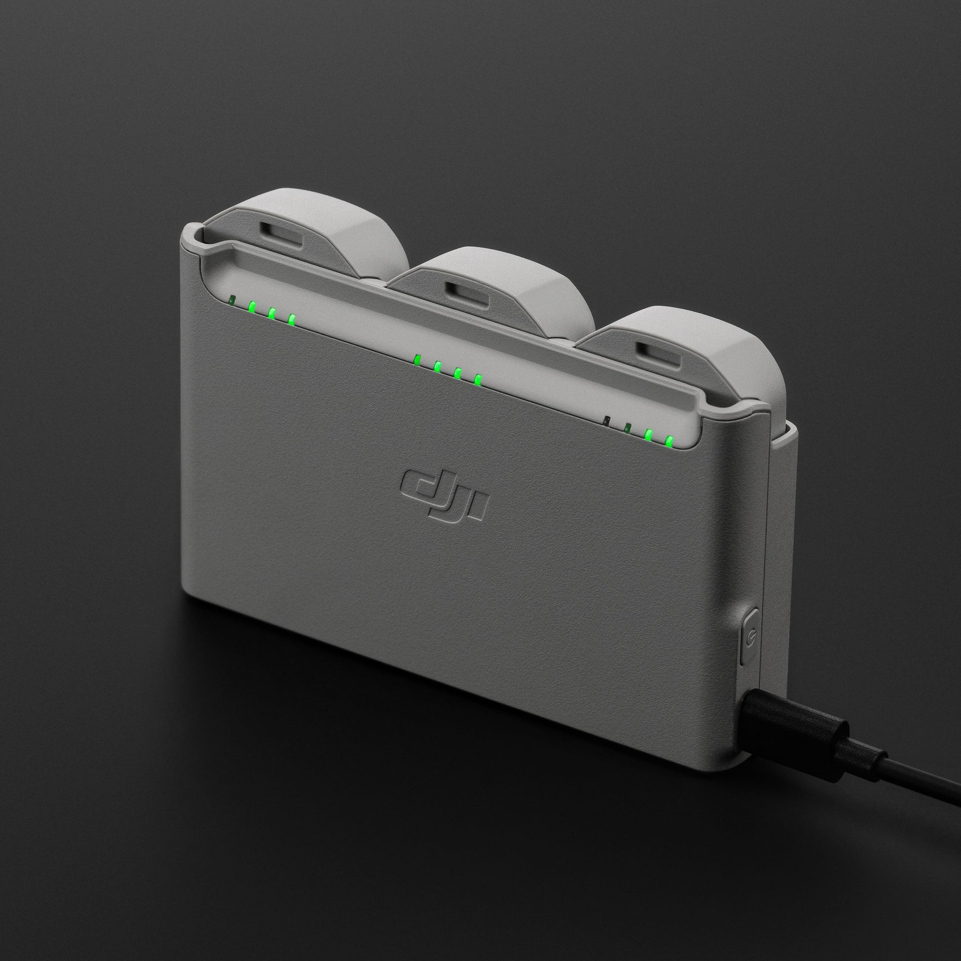 DJI Neo opladningsstation i grå til tre DJI Neo batterier med grønne indikatorlys og tilsluttet opladerkabel.