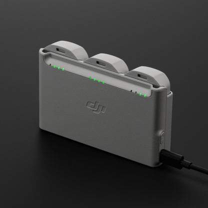 DJI Neo opladningsstation i grå til tre DJI Neo batterier med grønne indikatorlys og tilsluttet opladerkabel.