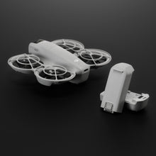 Grå DJI Neo drone med beskyttelsespropelbeskyttere og aftaget DJI Neo batteri på mørk overflade.