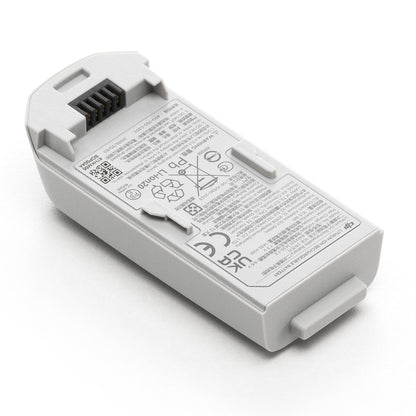 DJI Neo dronebatteri med sorte stikben og etiketter med sikkerhedsadvarsler, symboler og tekniske data på flere sprog.